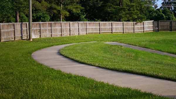 A walking path featuring well cut grass with a wooden fence in the distance
